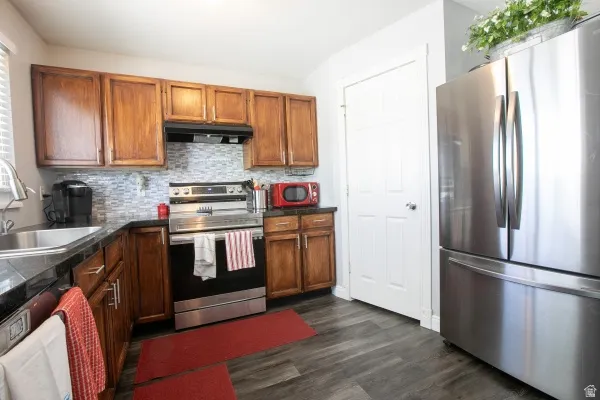 Kitchen with stainless steel appliances, dark countertops, dark wood-type flooring, backsplash, and wood finish cabinetry