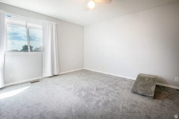 Carpeted empty room with baseboards and a ceiling fan