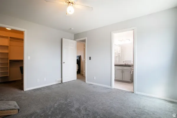 Unfurnished bedroom featuring light colored carpet, a walk in closet, ceiling fan, and ensuite bathroom