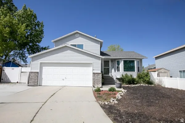 Traditional-style home featuring a garage, driveway, brick siding, and a gate