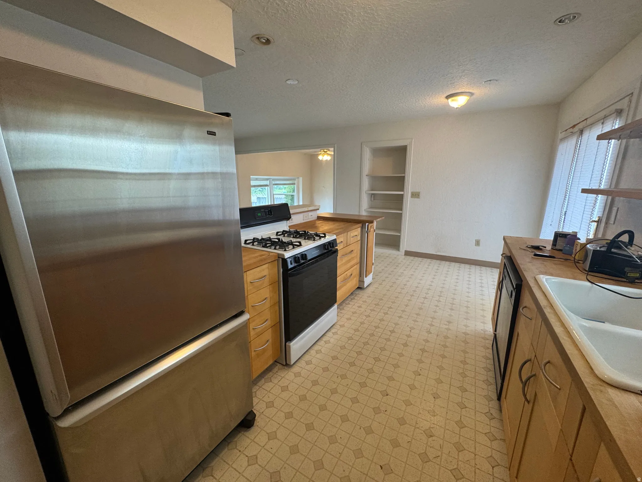 Kitchen featuring freestanding refrigerator, gas stove, light floors, a textured ceiling, and butcher block counters