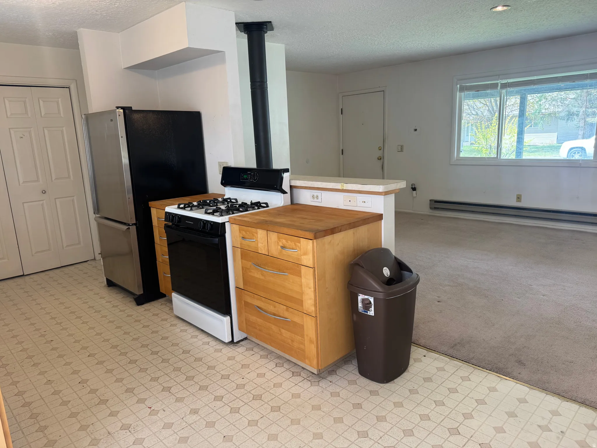 Kitchen featuring light flooring, range with gas cooktop, a textured ceiling, a baseboard heating unit, and wood finish cabinets