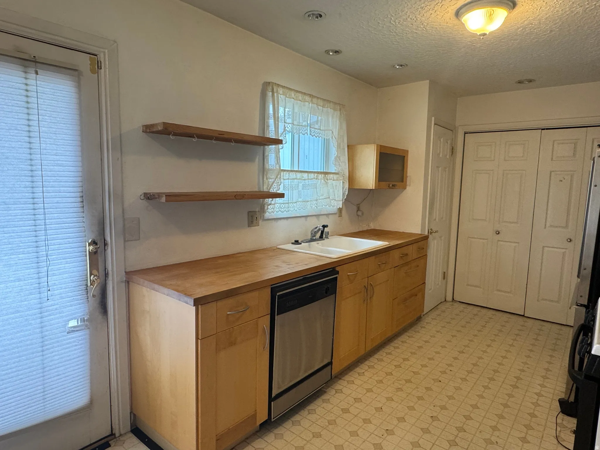 Kitchen with light floors, open shelves, dishwasher, a textured ceiling, and freestanding refrigerator