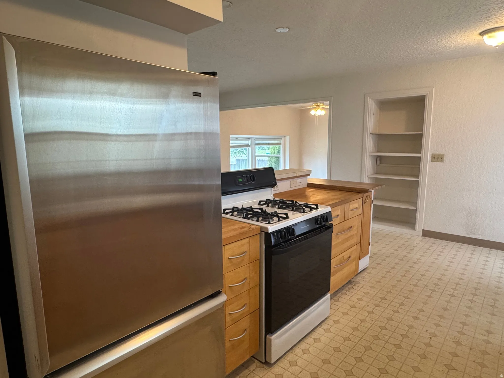Kitchen with freestanding refrigerator, range with gas stovetop, a textured ceiling, built in features, and a textured wall