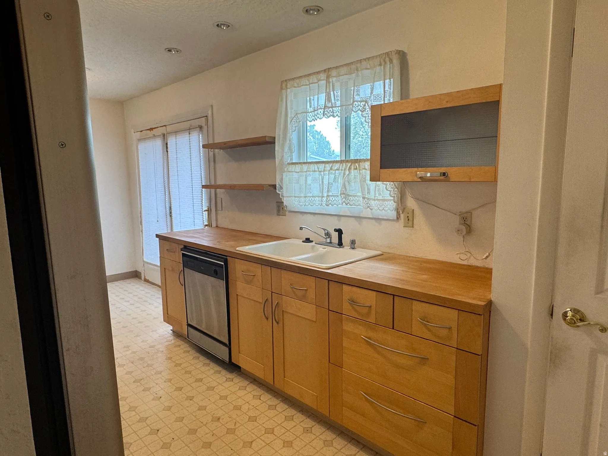 Kitchen featuring light flooring, butcher block countertops, open shelves, and dishwasher