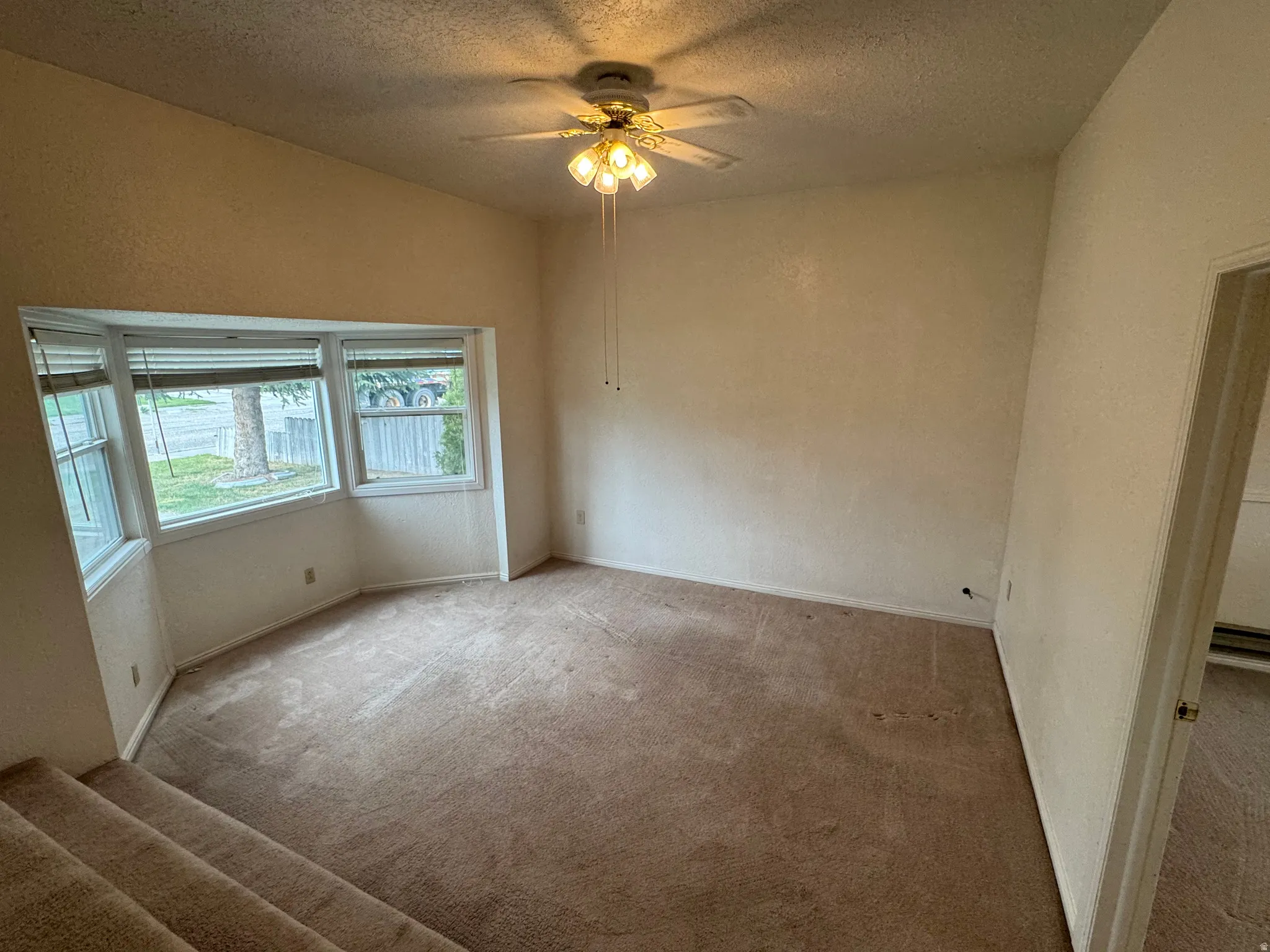 Carpeted spare room featuring a textured ceiling, a ceiling fan, and a textured wall