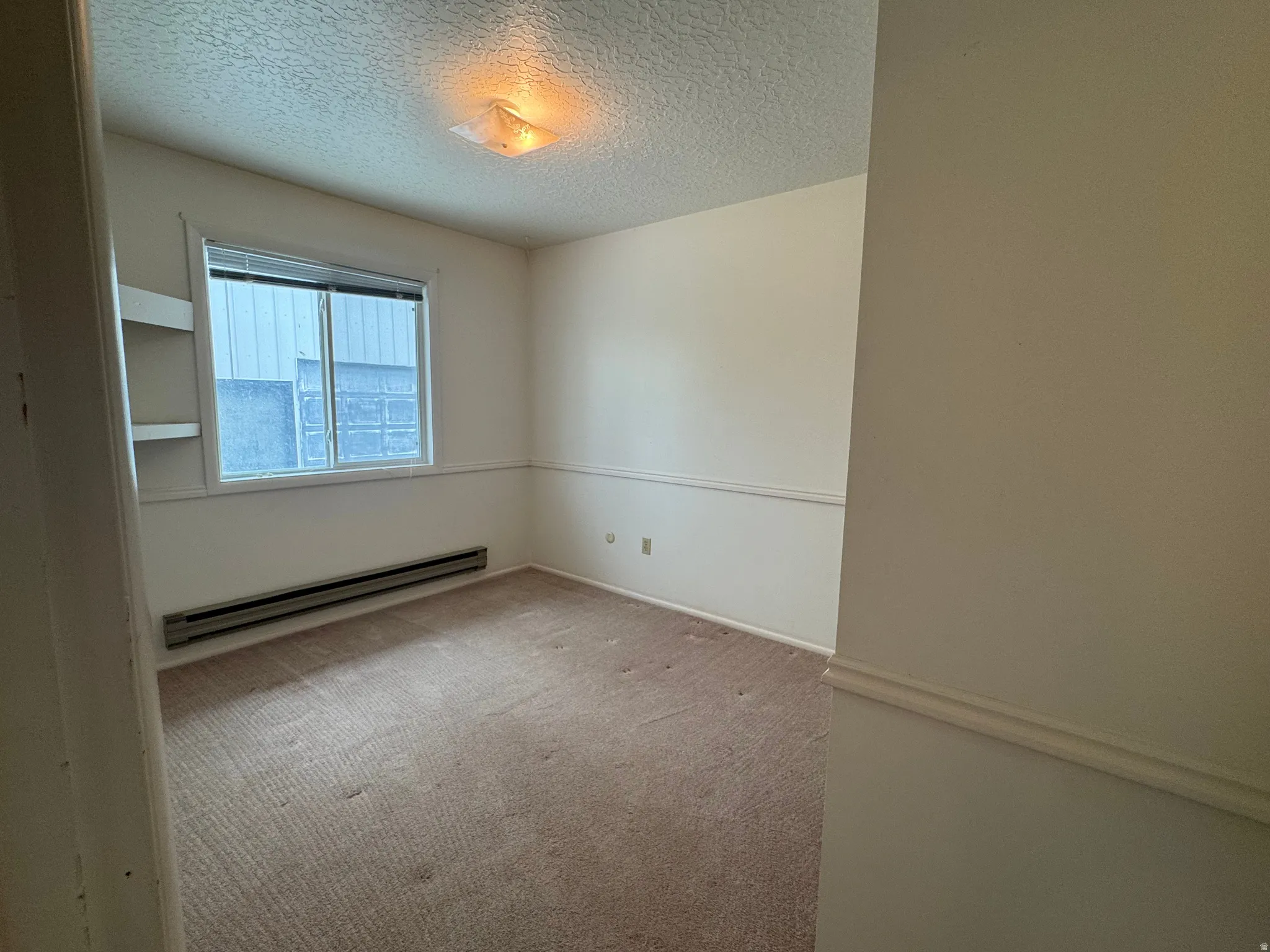 Empty room with a textured ceiling, light carpet, and a baseboard radiator