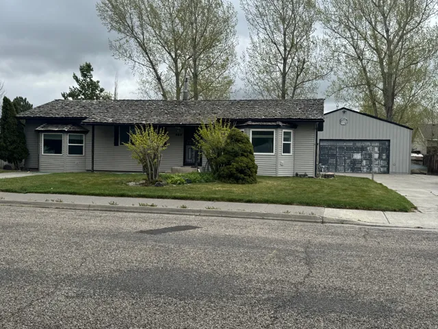 Ranch-style house featuring a front yard, driveway, covered porch, and an attached garage