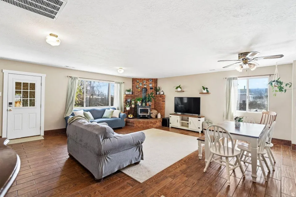 Living area featuring wood-type flooring, a wood stove, a ceiling fan, and a textured ceiling
