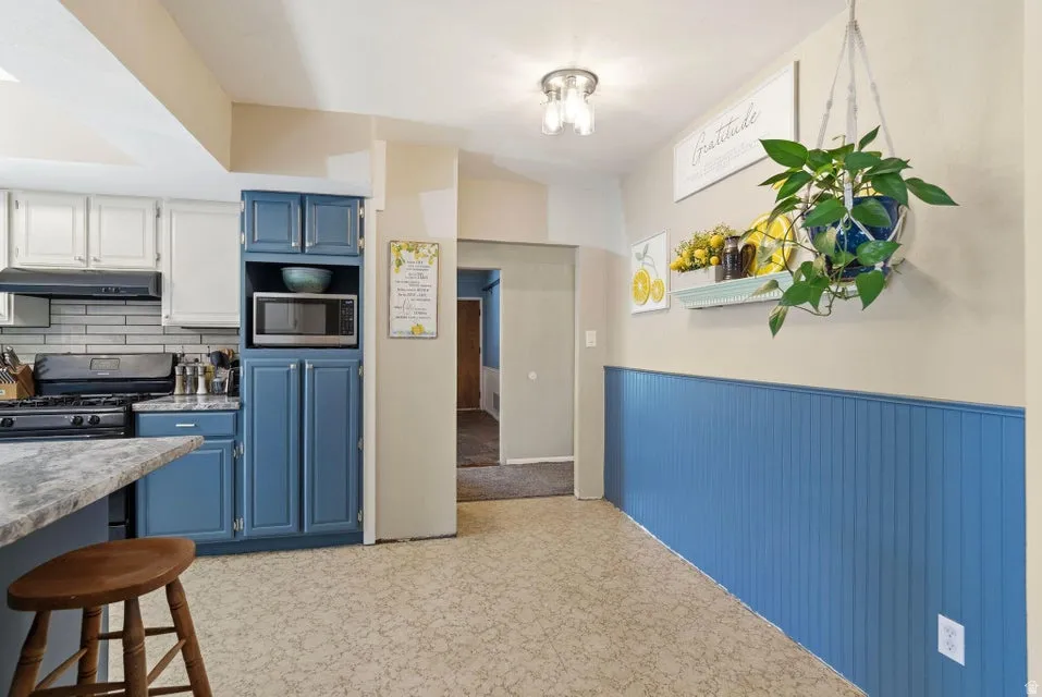 Kitchen featuring stainless steel microwave, light countertops, two tone cabinets, wainscoting, and backsplash