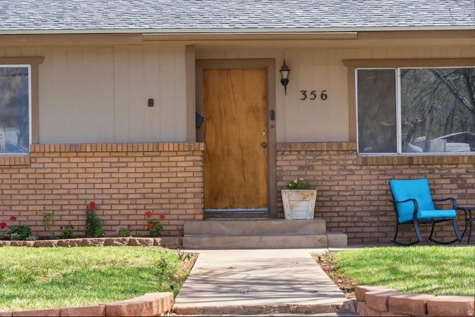 Doorway to property featuring brick siding and a shingled roof