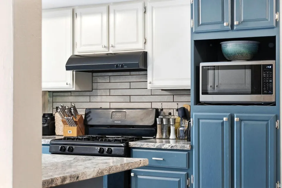 Kitchen featuring black gas stove, blue cabinets, stainless steel microwave, and white cabinets