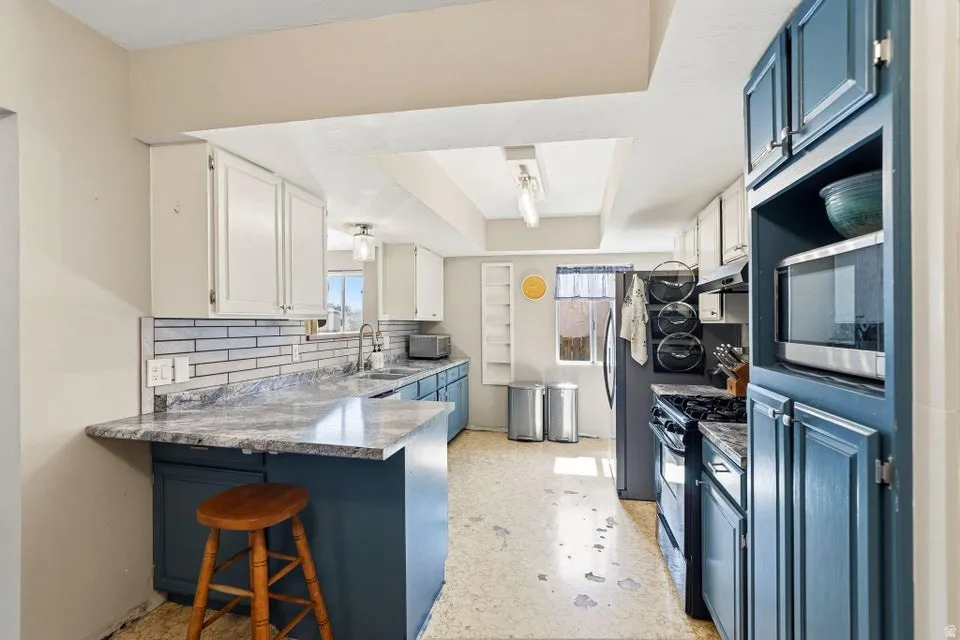 Kitchen featuring a kitchen bar, a peninsula, stainless steel appliances, blue cabinetry, and decorative backsplash