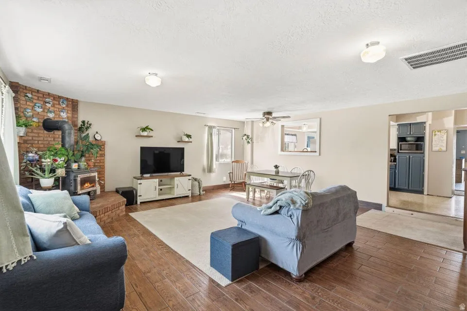 Living area featuring a wood stove, hardwood / wood-style floors, ceiling fan, and a textured ceiling