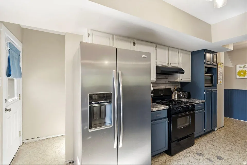 Dual tone kitchen with stainless steel appliances, a wainscoted wall, two tone cabinetry, light floors, and tasteful backsplash