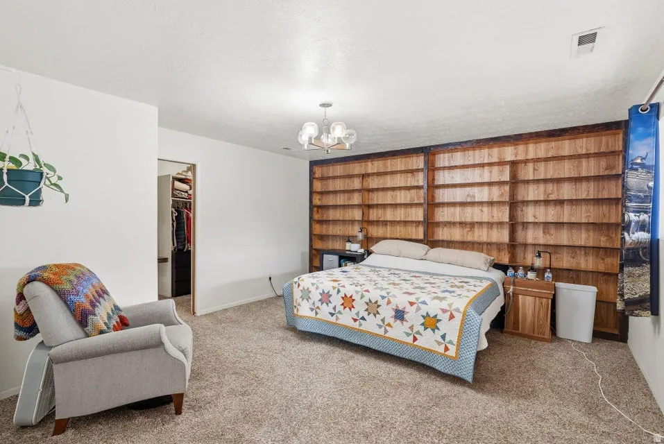 Carpeted bedroom with a walk in closet, suspended lighting, and a textured ceiling