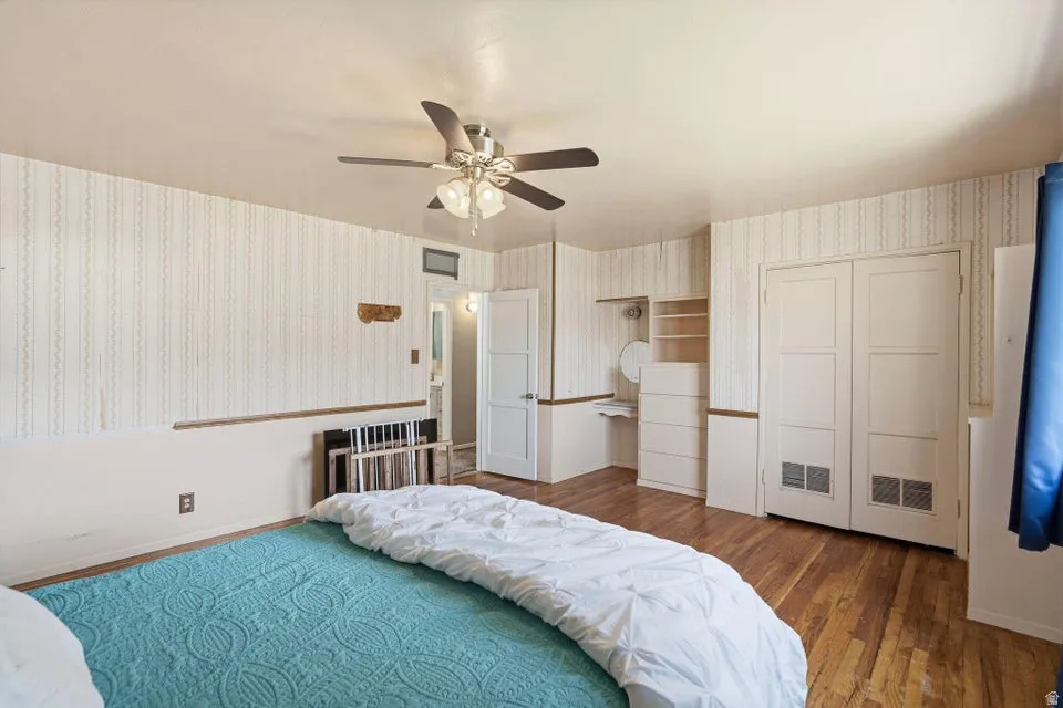 Bedroom featuring wallpapered walls, dark wood-type flooring, ceiling fan, and a closet