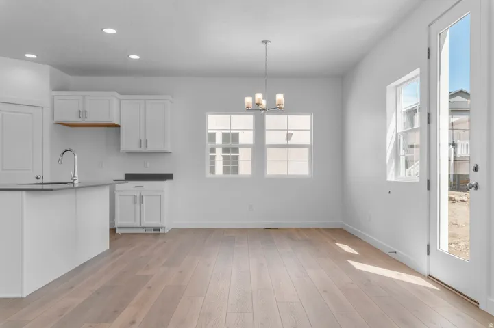 Open-concept kitchen and dining area featuring light wood-finish flooring, white cabinetry with dark countertops, a kitchen island with an integrated sink, and an elegant chandelier