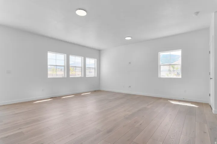 Spacious room featuring light wood-finish flooring, white walls, and multiple windows