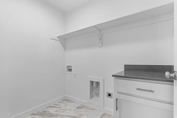 Utility room featuring a built-in white cabinet with a dark countertop, white walls, and a patterned tile floor