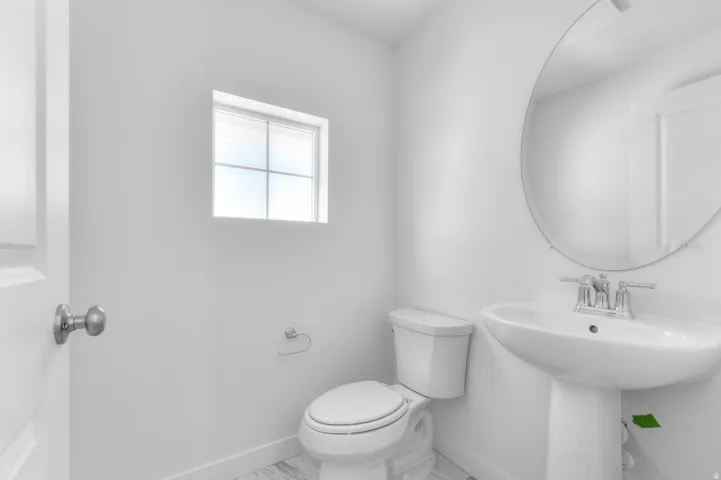 Bathroom featuring a pedestal sink, round wall mirror, and a window with horizontal blinds