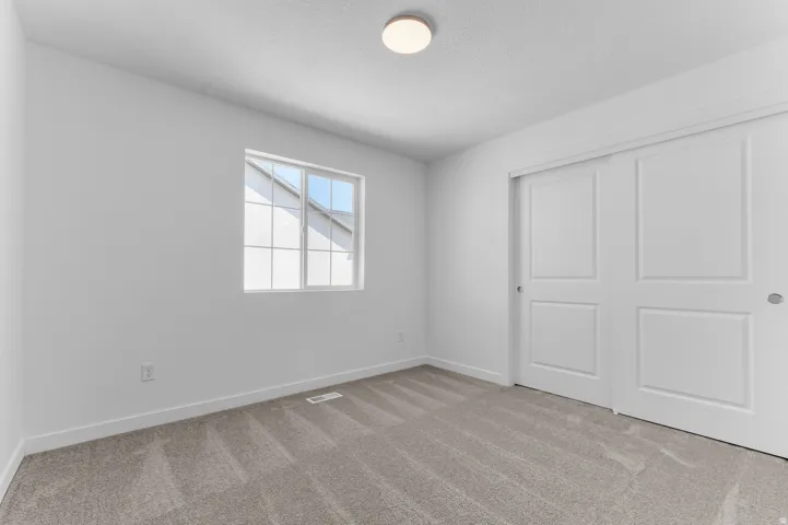 Bright room featuring a window with grid panes, textured carpeting, and a built-in closet with sliding panel doors