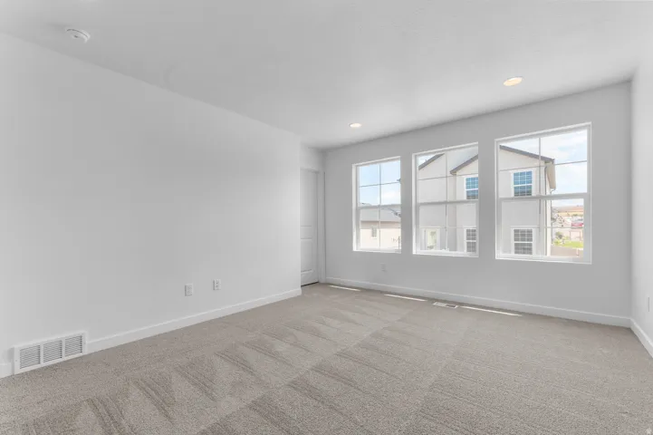 Bright interior space featuring three large windows, recessed ceiling lighting, textured carpet flooring, white baseboards, and a white interior door