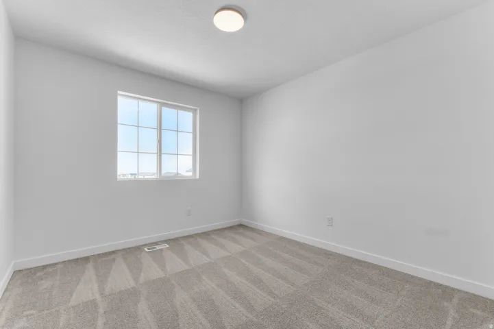 Bright room featuring a grid-pattern window, neutral-toned walls, textured carpet flooring, and a flush-mount ceiling light
