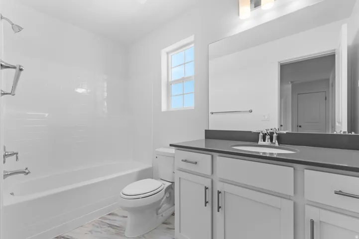 Full bathroom featuring a white tub/shower combination with subway tile surround, a single vanity with a dark countertop and undermount sink, a large wall-mounted mirror, and tile flooring