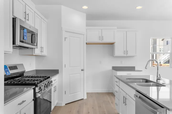 Modern kitchen featuring white shaker cabinetry, stainless steel appliances, dark countertops, and wood-finish flooring