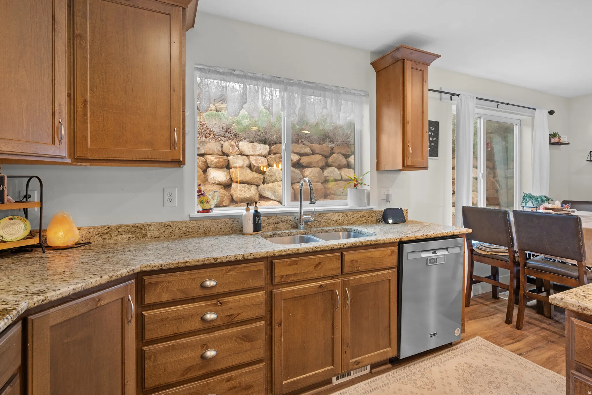 Kitchen featuring wood finish cabinets, stainless steel dishwasher, light stone countertops, and light wood finished floors