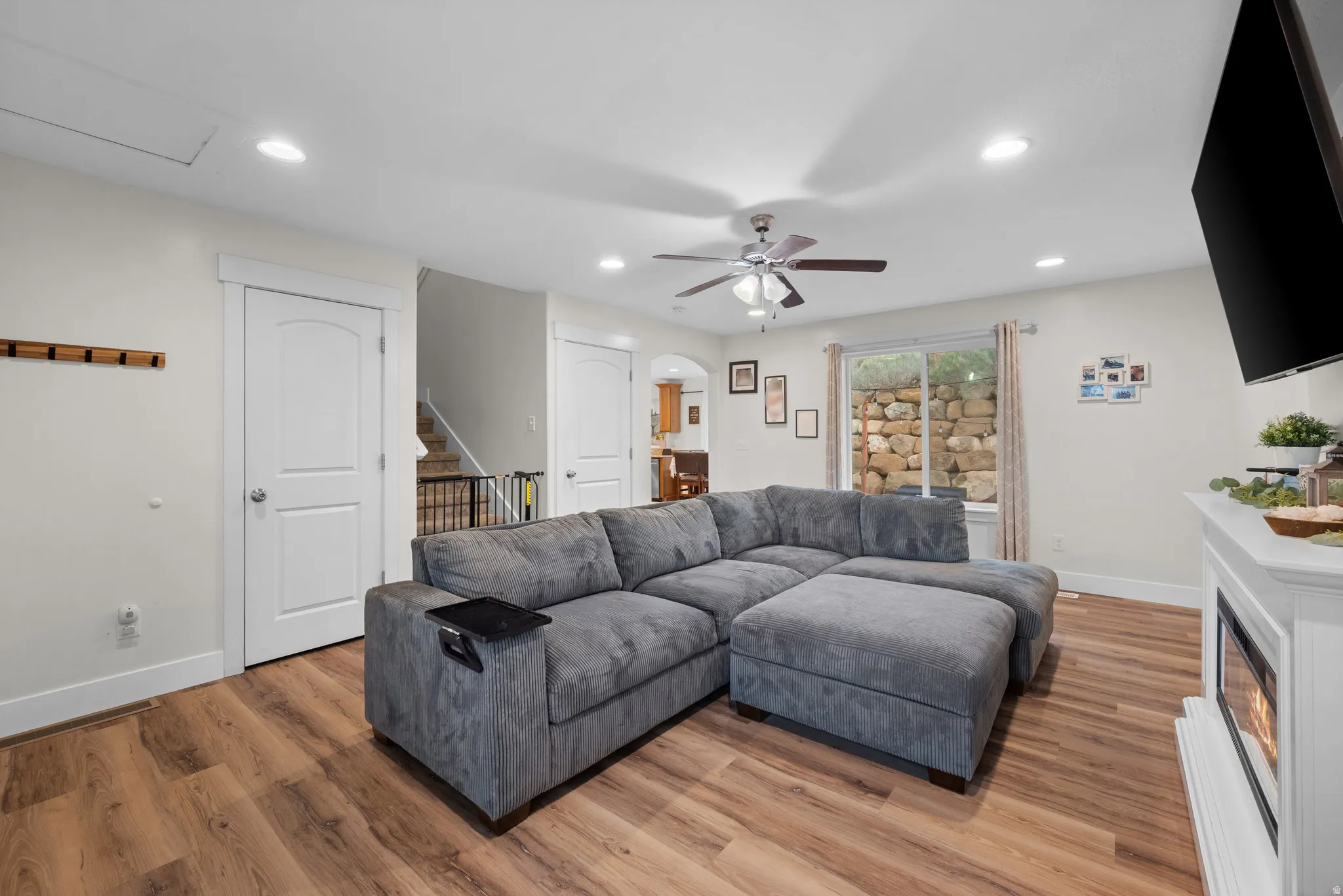 Living room featuring light wood finished floors, arched walkways, a ceiling fan, recessed lighting, and a glass covered fireplace