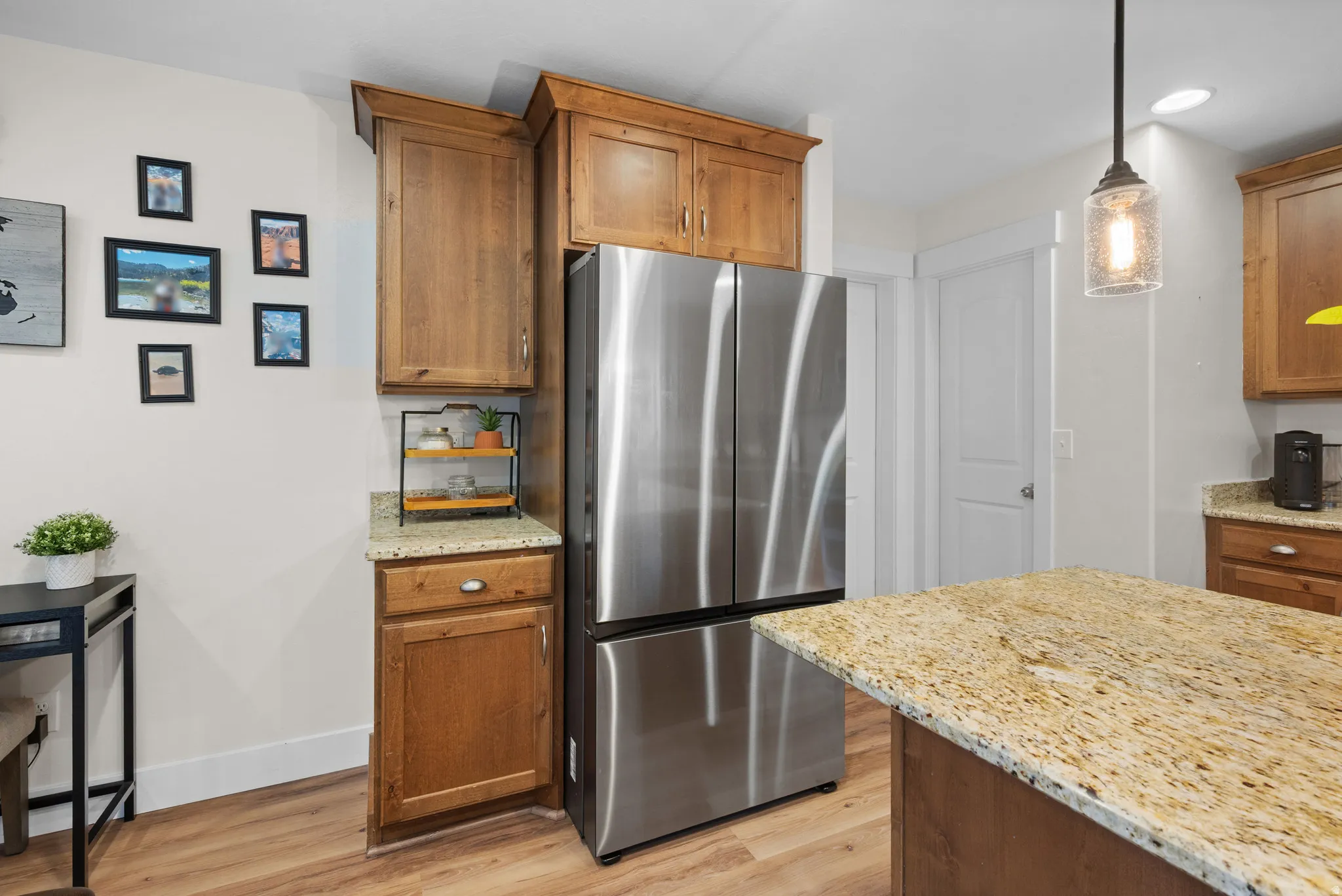 Kitchen featuring freestanding refrigerator, light stone countertops, light wood finished floors, pendant lighting, and wood finish cabinetry