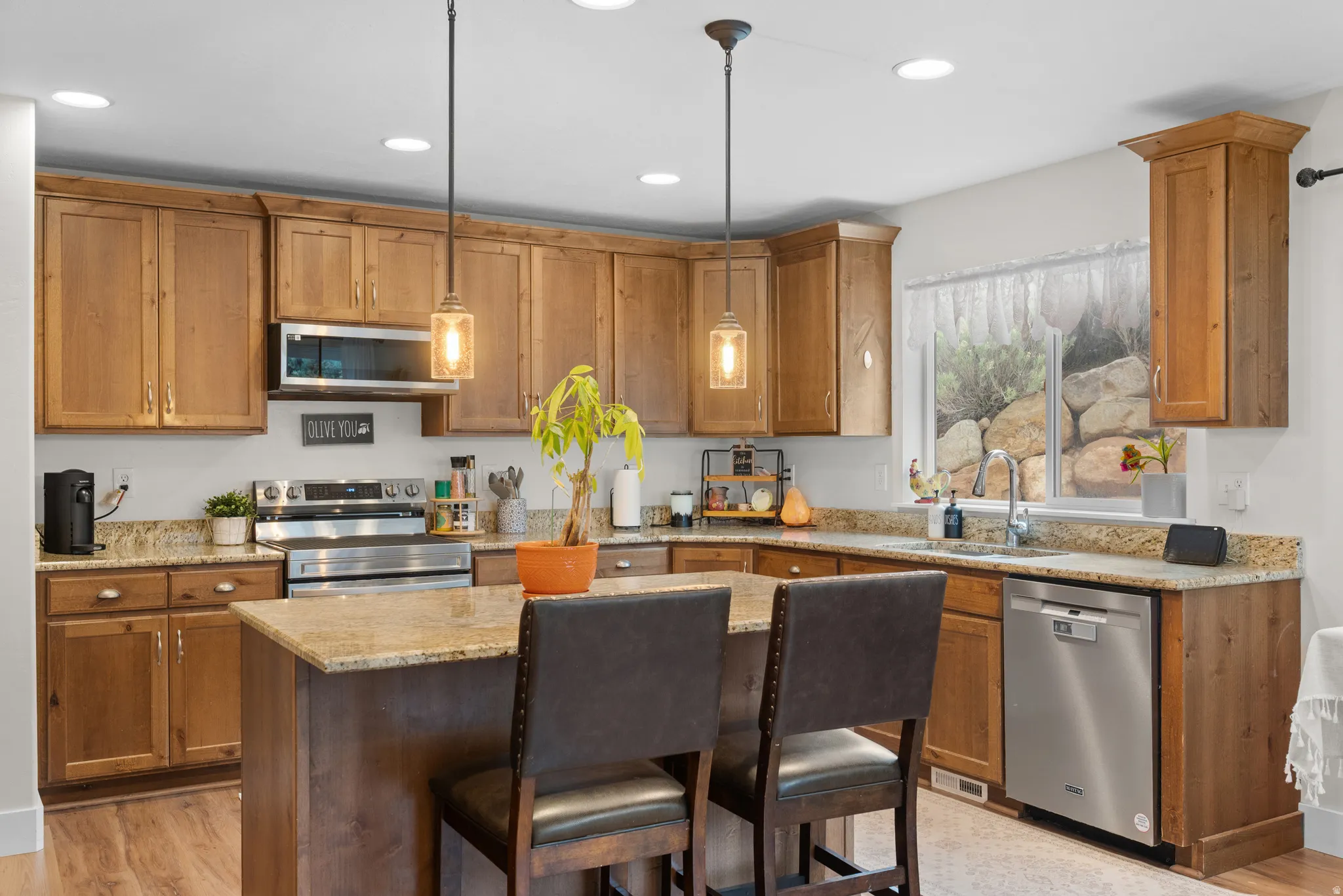 Kitchen with wood finish cabinetry, light stone counters, a kitchen breakfast bar, stainless steel appliances, and decorative light fixtures