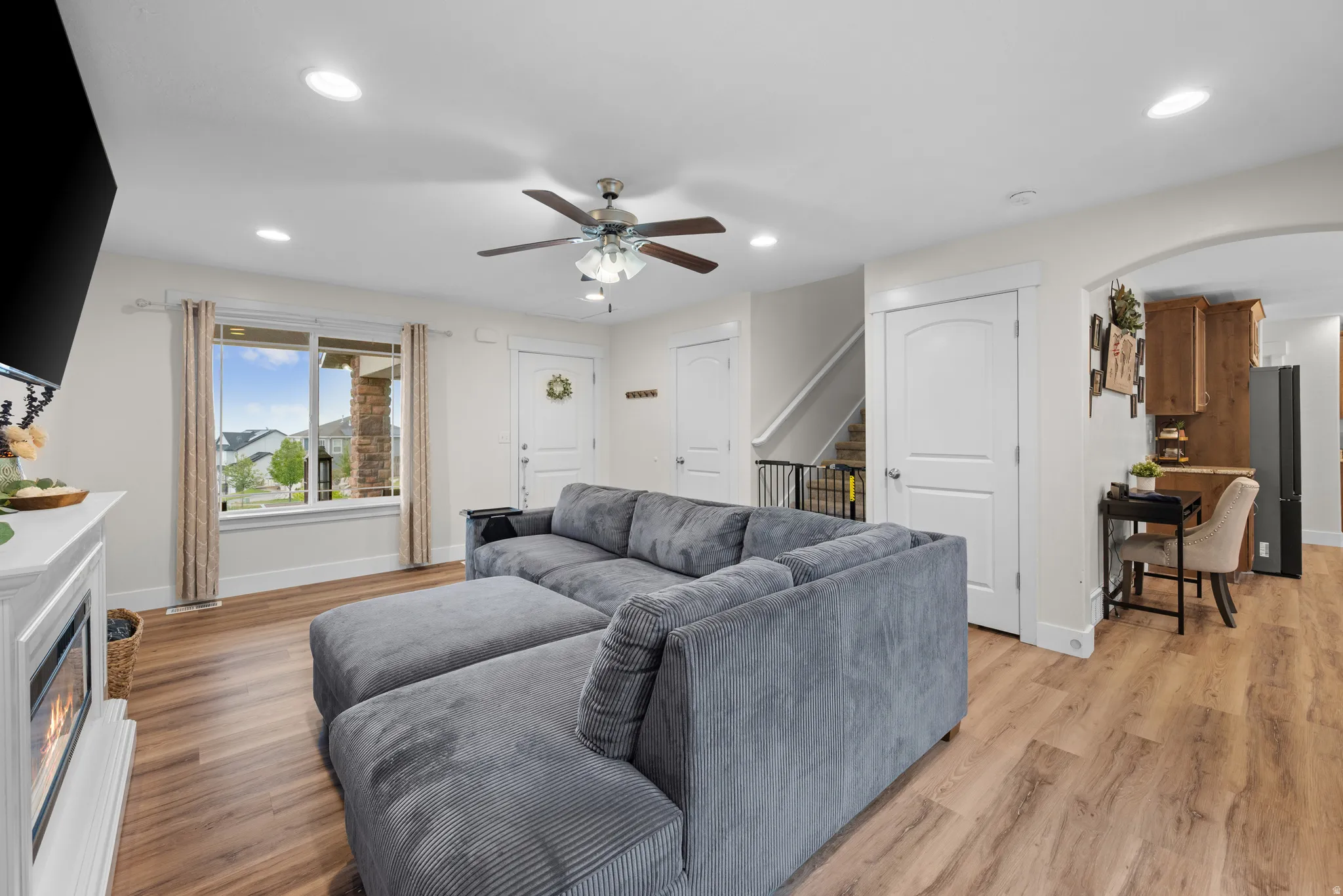Living room featuring light wood finished floors, ceiling fan, a glass covered fireplace, recessed lighting, and arched walkways
