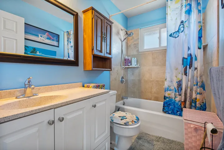Bathroom featuring a single vanity with an integrated sink, a built-in medicine cabinet, a bathtub with a shower, and tiled shower walls