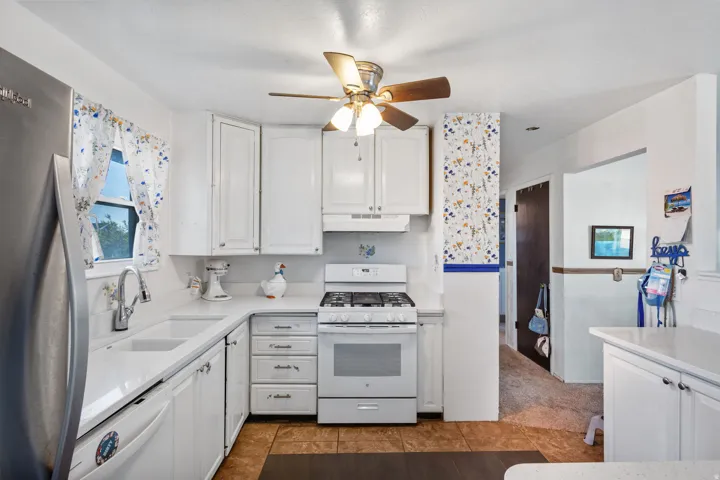Bright kitchen featuring white cabinetry, a double basin sink, white countertops, a gas range with an overhead vent, and wood-finish flooring