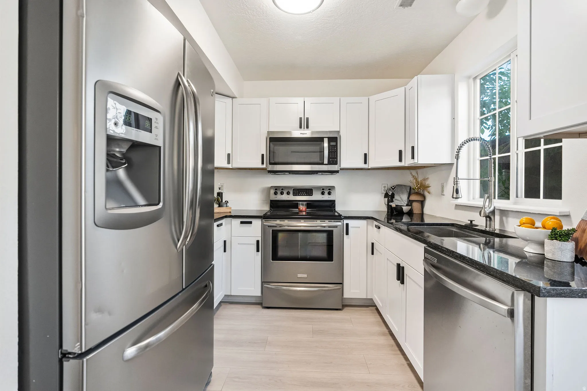 Kitchen with stainless steel appliances, white cabinets, dark stone countertops, and light wood-style flooring