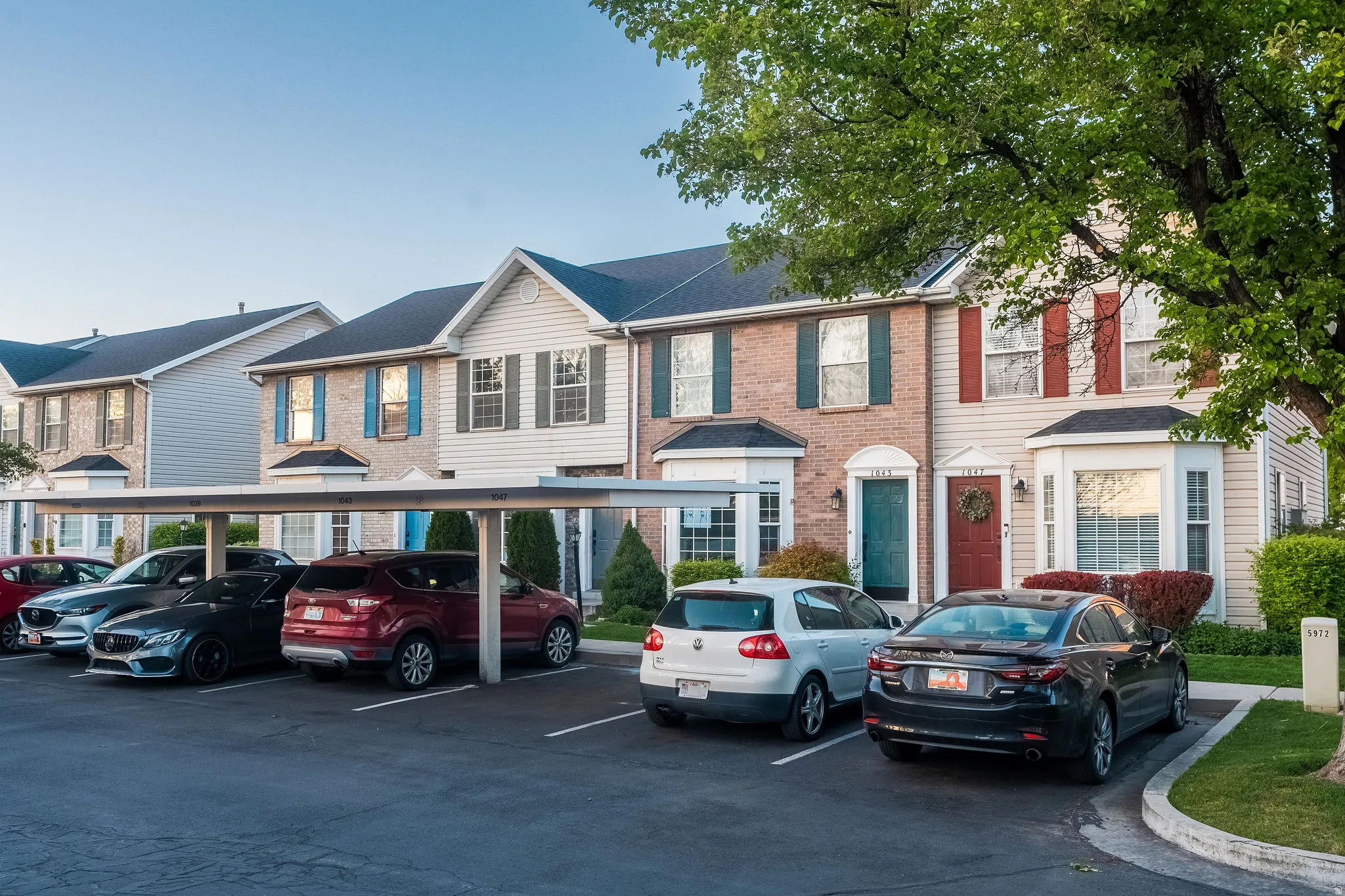 Colonial house featuring covered and uncovered parking, brick siding, a residential view, and a shingled roof