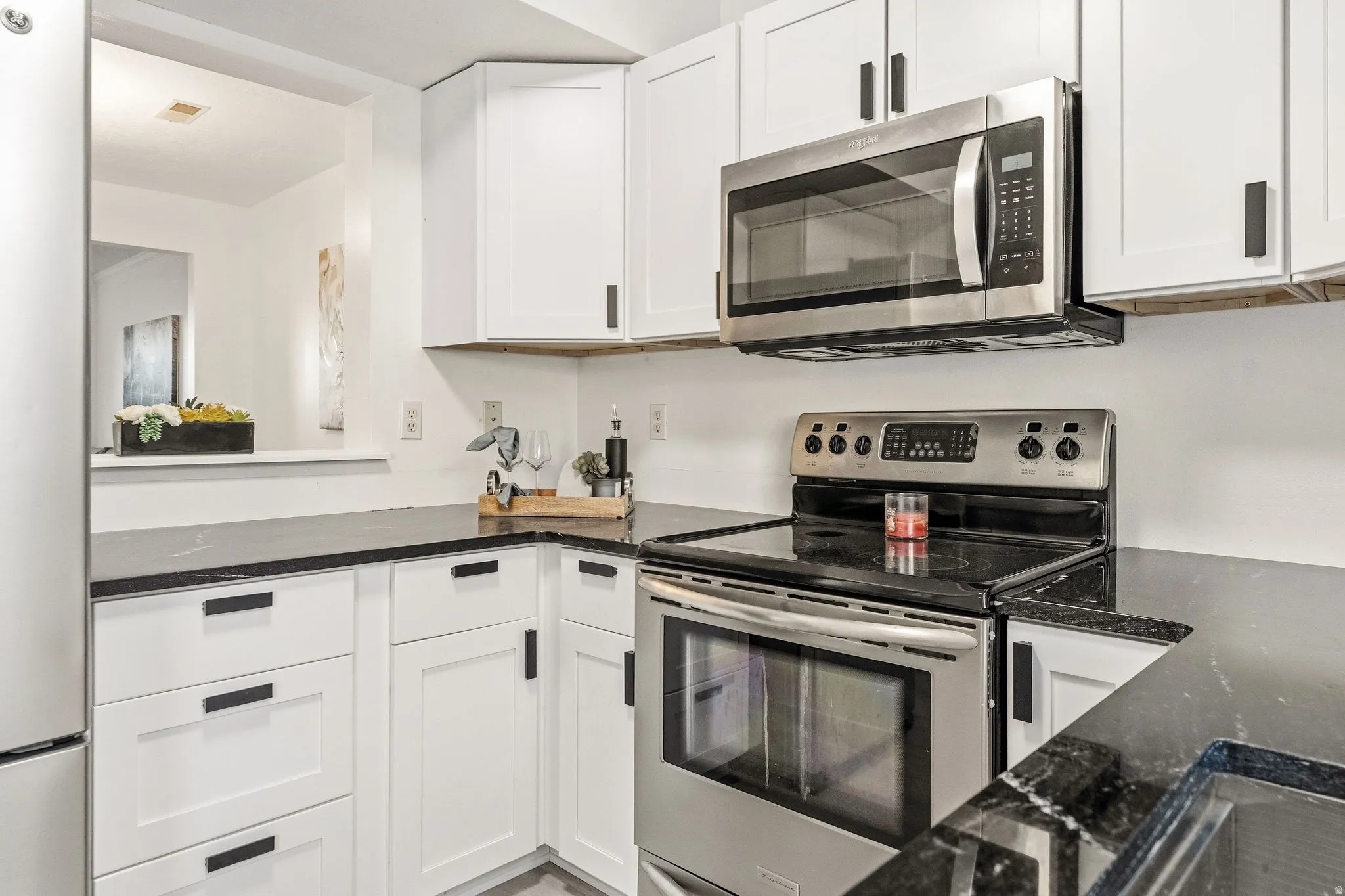 Kitchen featuring stainless steel appliances, white cabinets, and dark stone counters