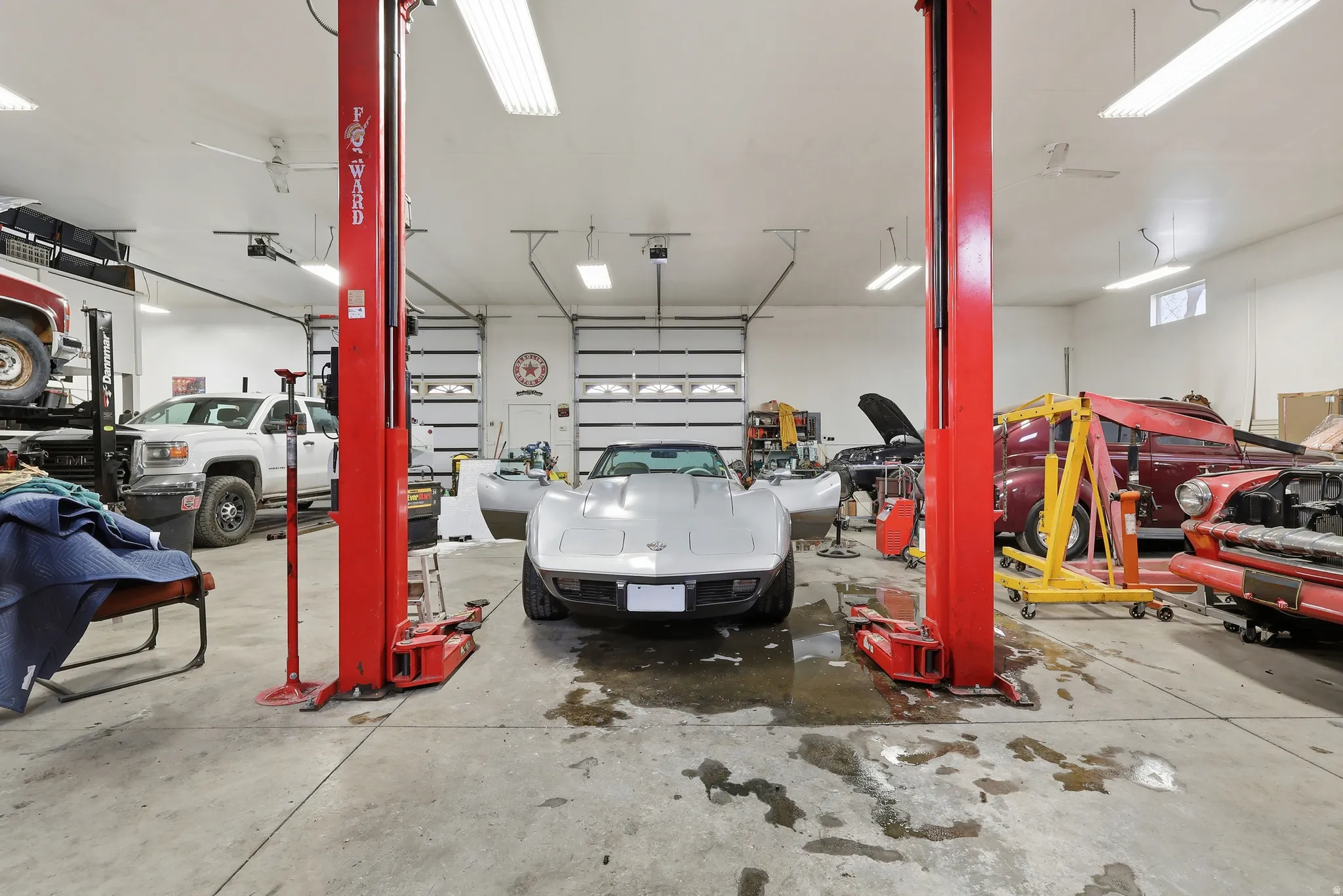 Spacious garage featuring a concrete floor, two vehicle lifts, multiple overhead garage doors, bright ceiling-mounted strip lighting, and transom windows