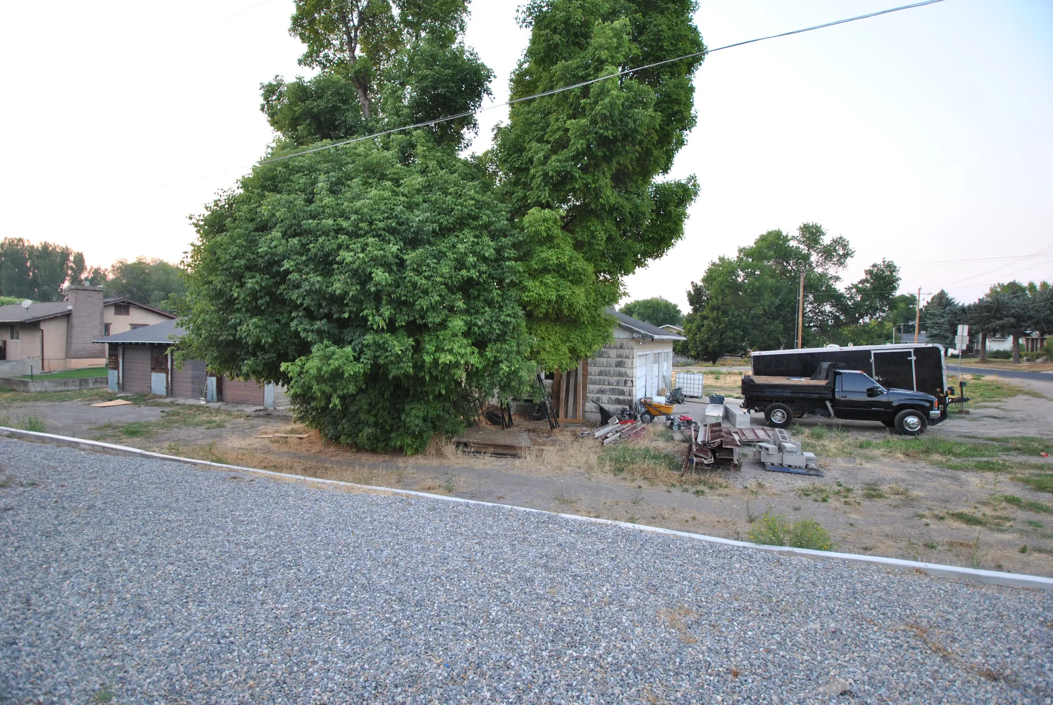 Gravel surface entrance area with mature trees and a block-built structure