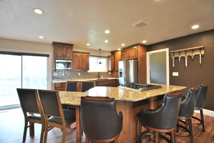 Kitchen featuring dark wood-style flooring, decorative backsplash, light stone counters, and stainless steel appliances.  The side table can be a dining room table or an extension to the countertop