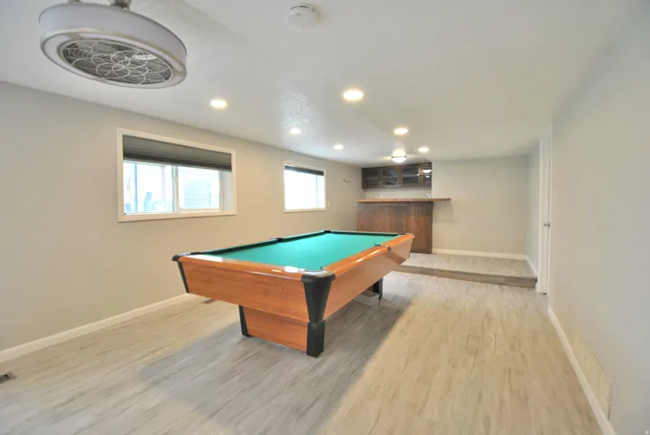 Family room with light wood-style flooring, recessed lighting, pool table (included), and wet bar beyond.