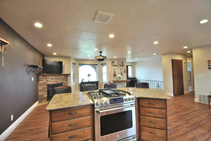 Kitchen featuring open floor plan, stainless steel gas range oven, light stone countertops, dark wood-style floors, and recessed lighting