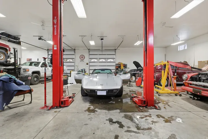 Spacious garage featuring a concrete floor, two vehicle lifts, multiple overhead garage doors, bright ceiling-mounted strip lighting, and transom windows