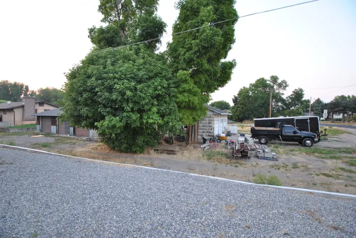 Gravel surface entrance area with mature trees and a block-built structure