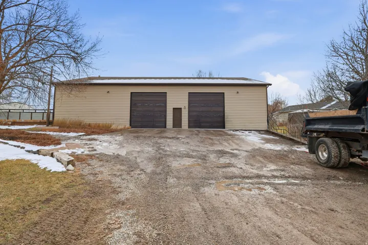 Detached beige siding structure featuring two roll-up doors and a separate entry door