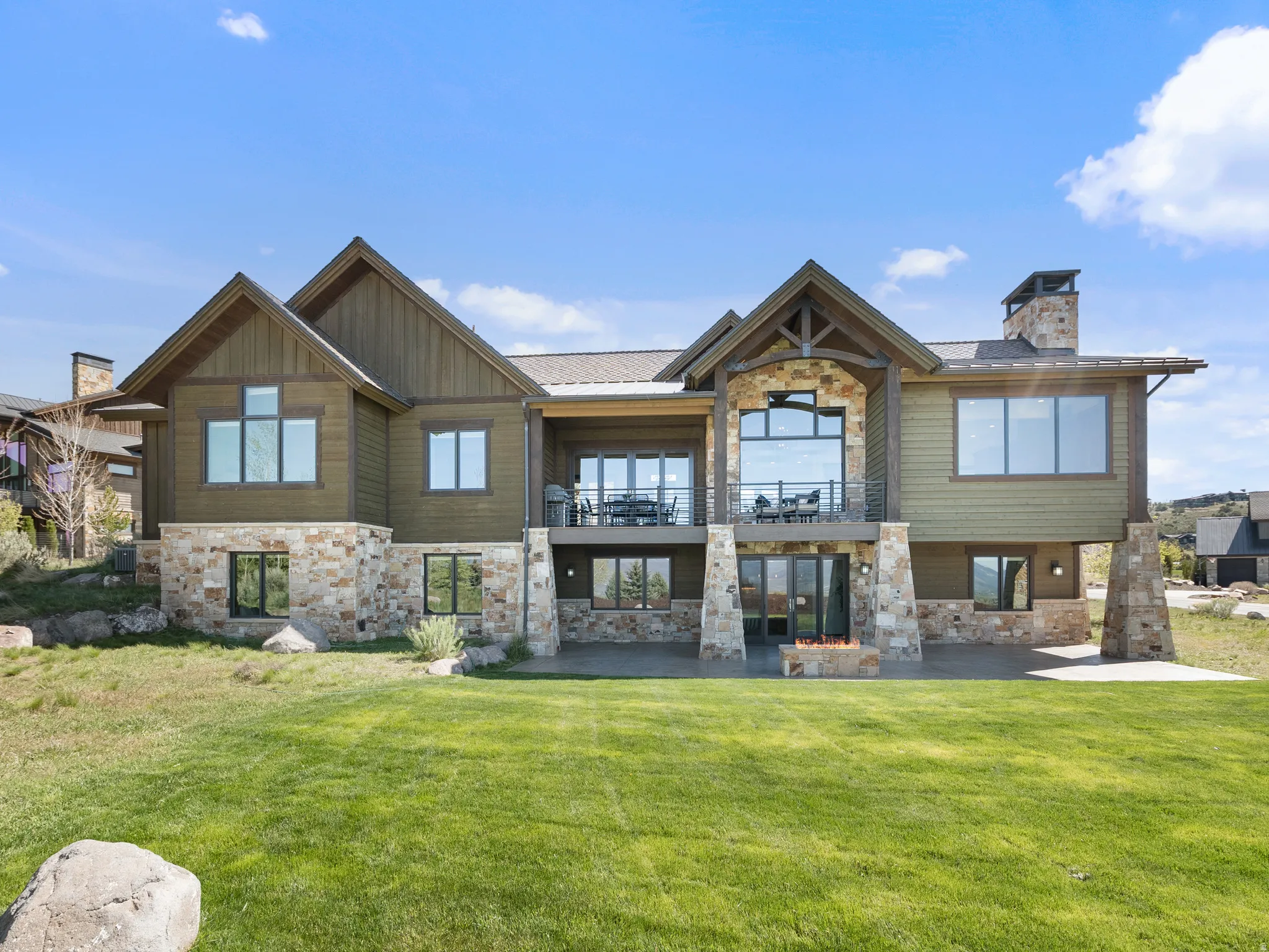 Back of house featuring stone siding, a balcony, and a yard