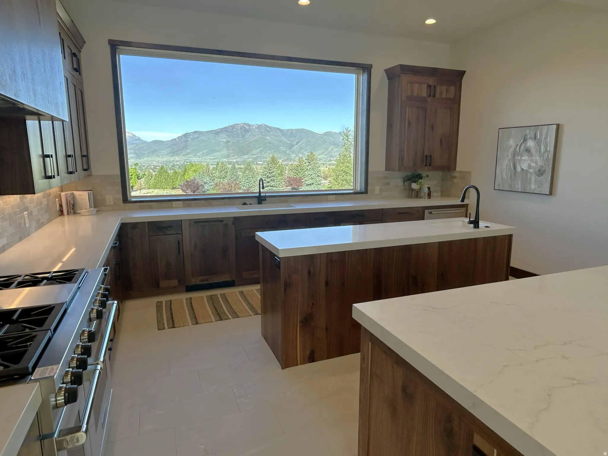 Expansive kitchen featuring a large picture window, two central islands with stone countertops, wood-finish cabinetry, and a professional-grade range